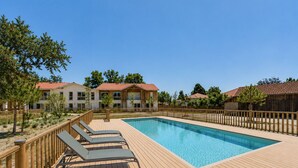 A swimming pool with wooden deck and lounge chairs, surrounded by buildings with red-tiled roofs. - Le Nose Rider - studio for 3 - shared pool (Biscarrosse)