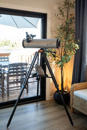 A telescope on a tripod in a room with a view of the outdoors.