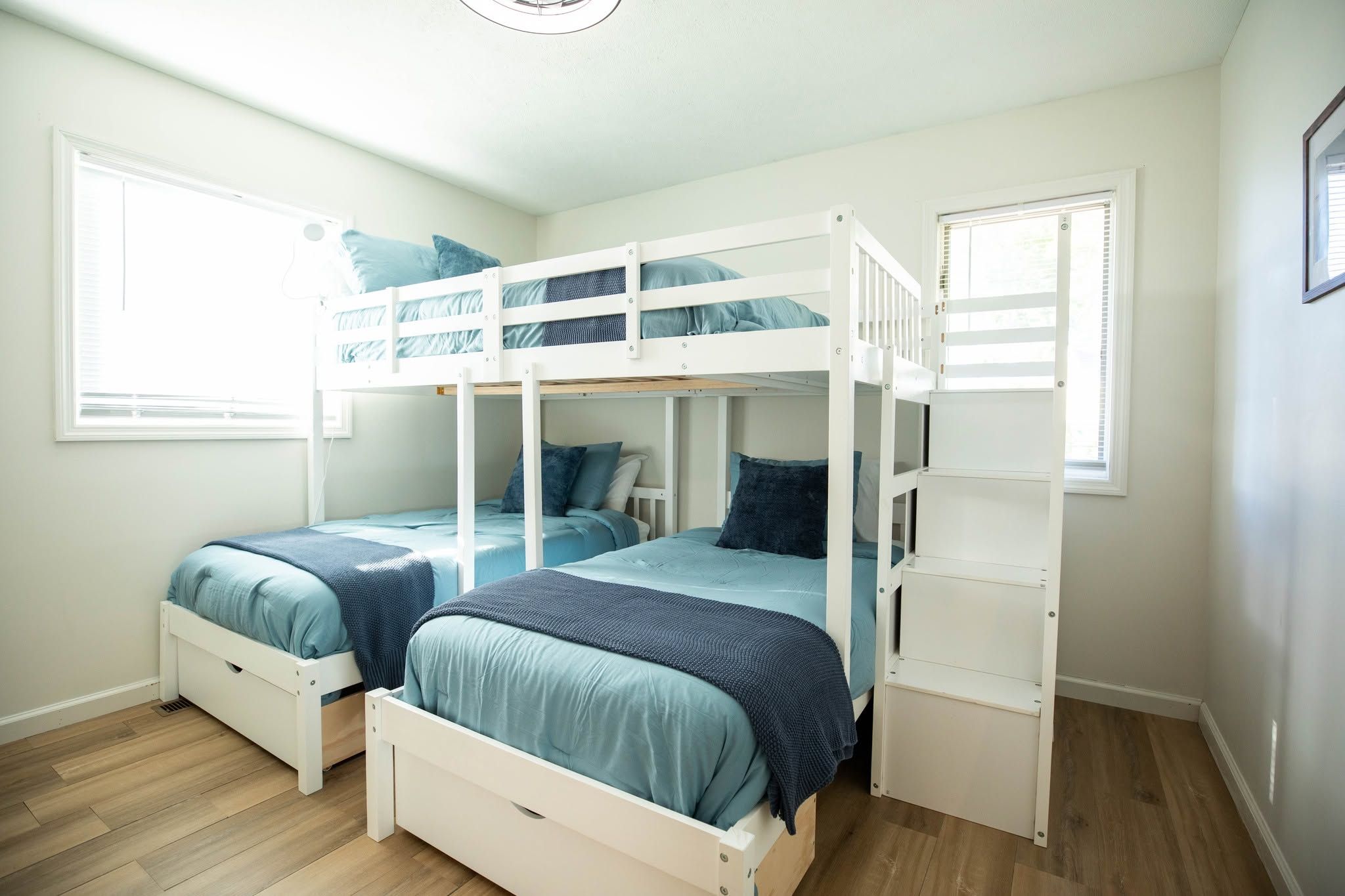 A room with two bunk beds, each with a mattress and pillows, and a small drawer under one bed.