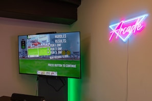 A racing game on a TV screen with a neon sign reading 'Arcade' in the background. - Sunrise on Sawmill - Kayaks, Paddleboat, Firepit, Arcade! (Leesburg)