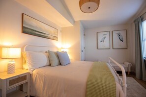 Un dormitorio con cama, lámparas de noche, mesita de noche y un cuadro colgado en la pared, además de una ventana con cortinas.