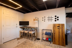 Une pièce avec une porte blanche, un bureau avec un ordinateur, deux chaises, un lampadaire, un mur orné d’œuvres d’art abstrait et un meuble en bois.