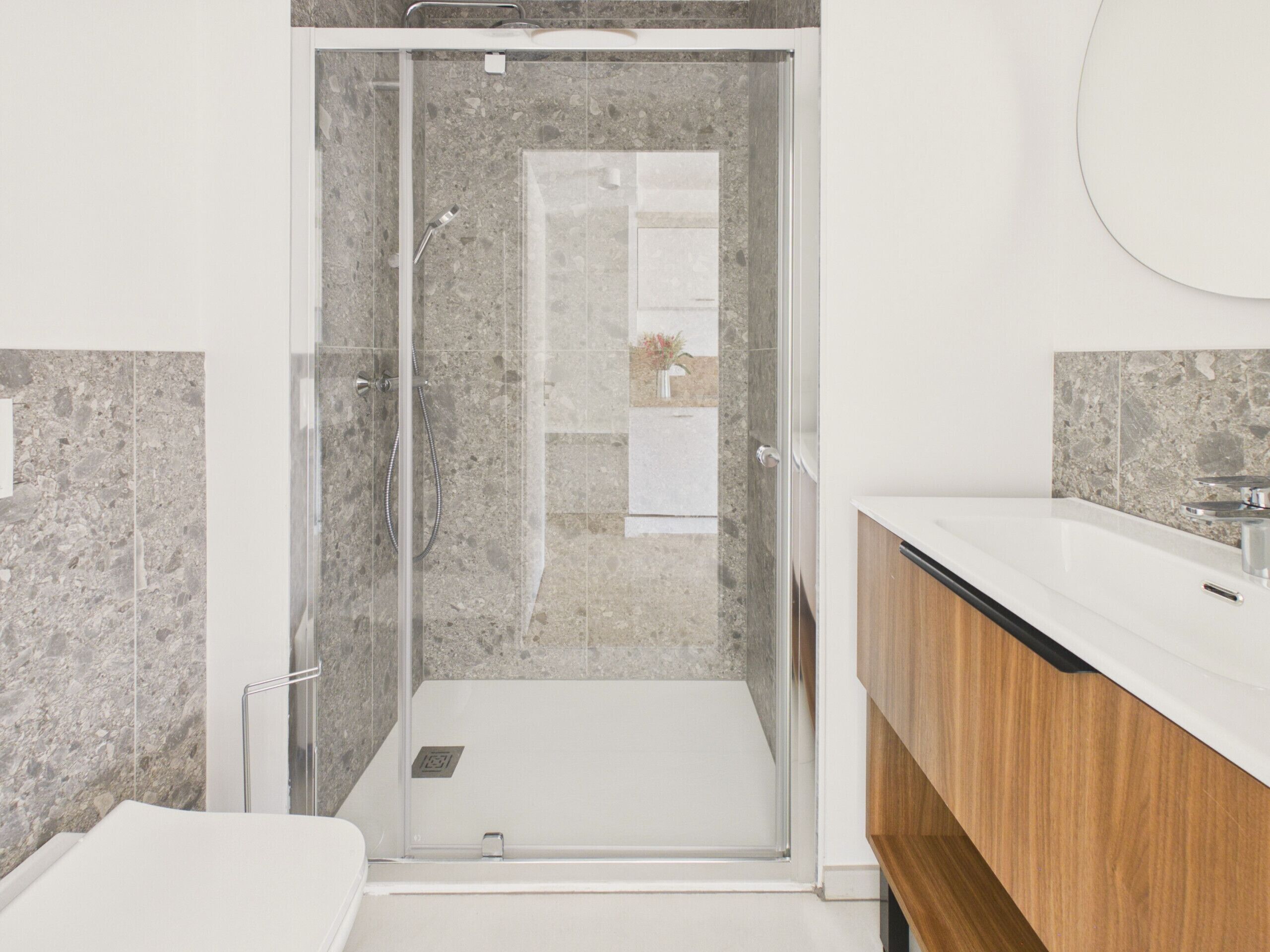 A modern bathroom with a glass-enclosed shower, a white sink, and a wooden vanity.