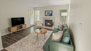 A living room with a flat-screen TV, a fireplace, a sofa, and a coffee table. - Green & Private 2BR King Bed/Pool/Gym Near UAB/Hospitals (Homewood)