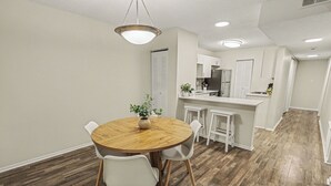 A modern kitchen with white cabinets, a wooden dining table, and a central island. - Green & Private 2BR King Bed/Pool/Gym Near UAB/Hospitals (Homewood)