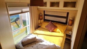 Een knus slaapkamer met een bed, nachtlampjes, een raam en een plafondlamp.