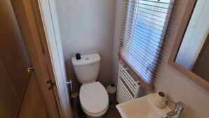 Een kleine badkamer met toilet, wastafel en raam met zonwering.