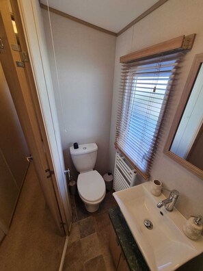 A compact bathroom with a toilet, sink, and window with blinds. - Unwind in our stunning premium waterside retreat. Full wraparound decking (Humberston)