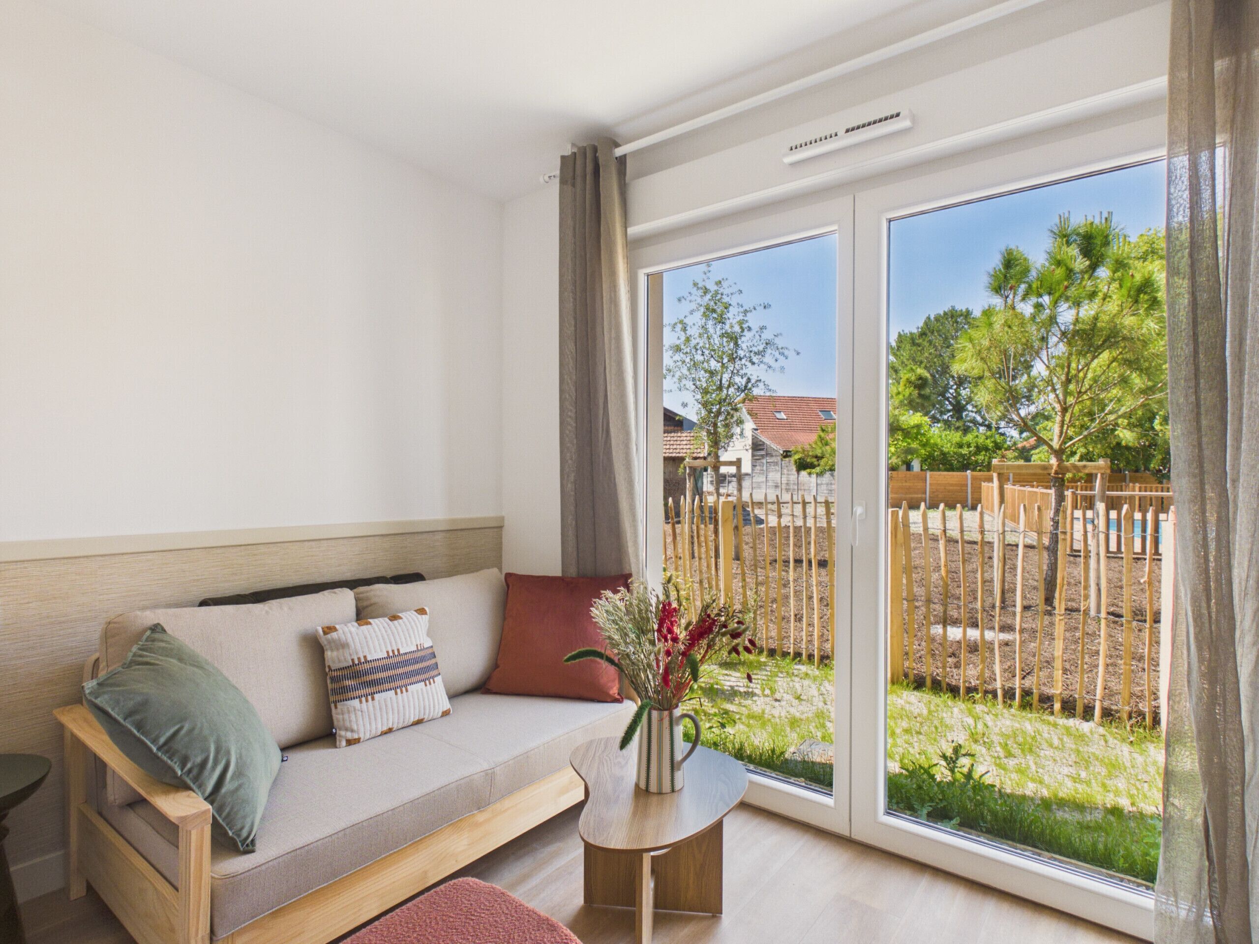 Ein modernes Zimmer mit einer Couch, einem kleinen Tisch und Blick auf einen umzäunten Garten.
