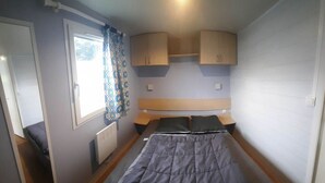 Ein Schlafzimmer mit Bett, einem Fenster mit Vorhängen, einem Heizkörper und Einbauschränken.