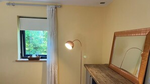 Een kamer met raam, vloerlamp, houten bureau en spiegel.