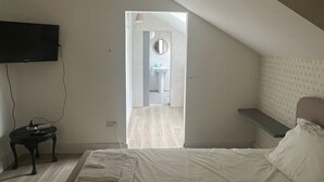 Een slaapkamer met een bed, een flatscreen-tv, een nachtkastje en uitzicht op een badkamer door een geopende deur.