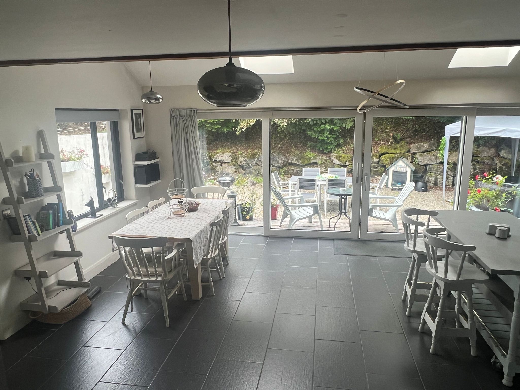 A dining area with a table and chairs, a bookshelf, and a view of the outdoors through large glass doors.