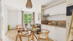 Una cuina moderna amb armaris blancs, una zona de menjador amb cadires de fusta i una finestra gran amb vista a vegetació.