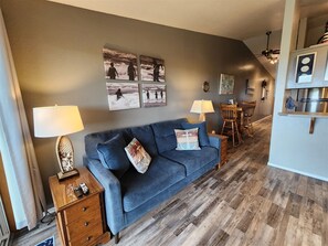 Ein Wohnzimmer mit blauem Sofa, Holzboden, Wandlampen und Kunstwerken.