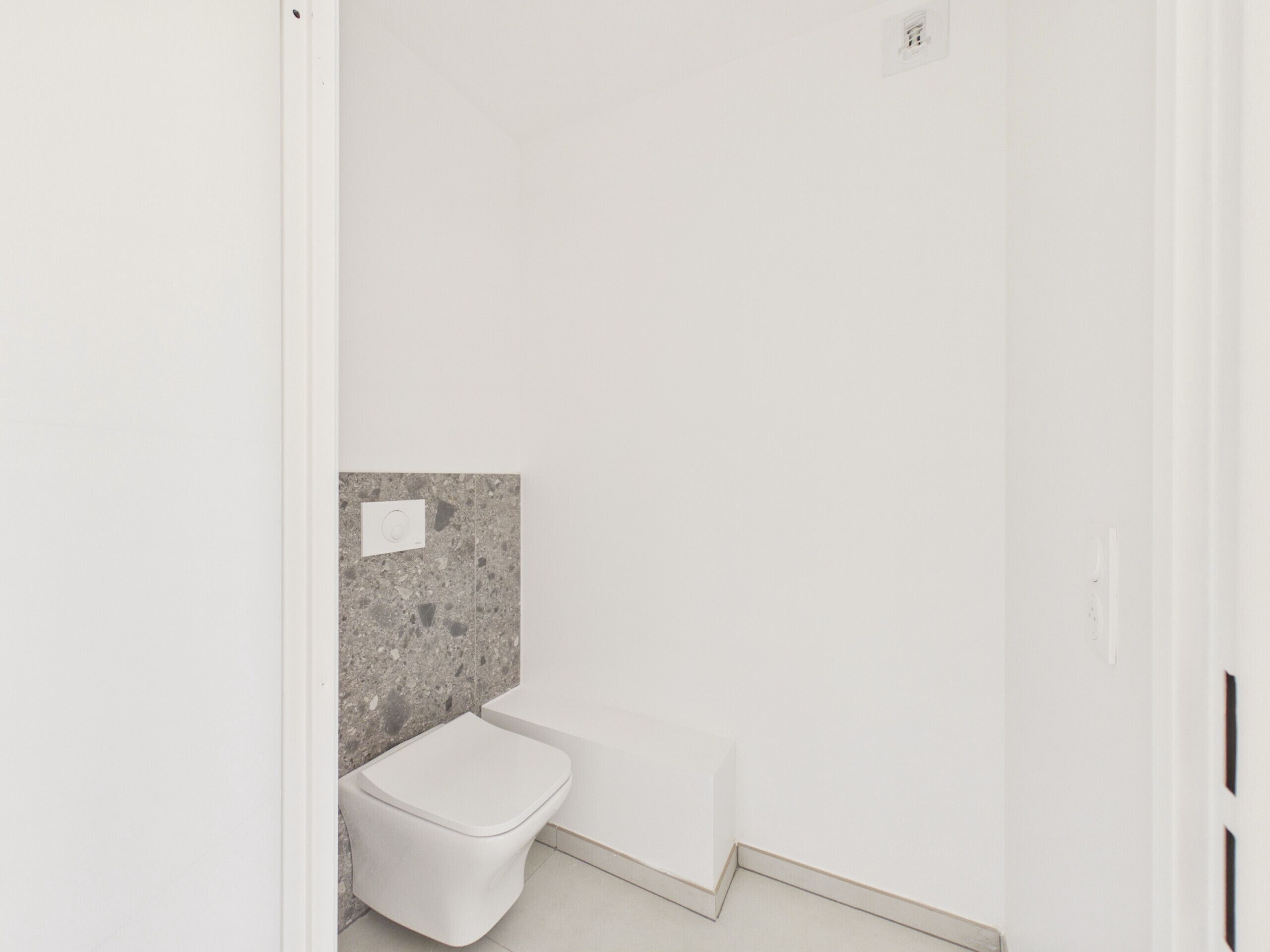 Et lille badeværelse med hvide fliser, toilet, badekar og bordplade i granit.