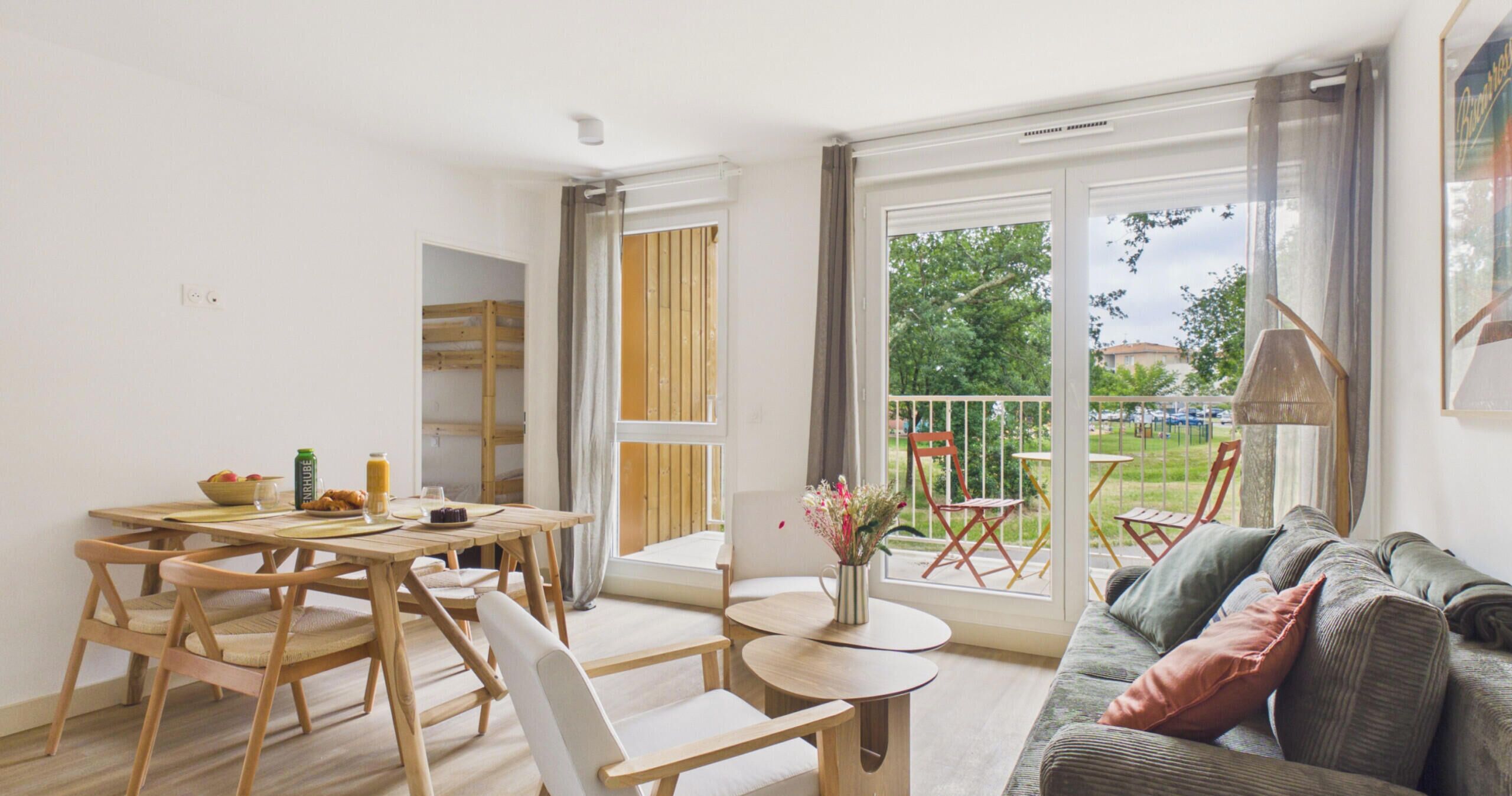 A modern living room with a sofa, dining table, chairs, and a balcony with outdoor furniture.