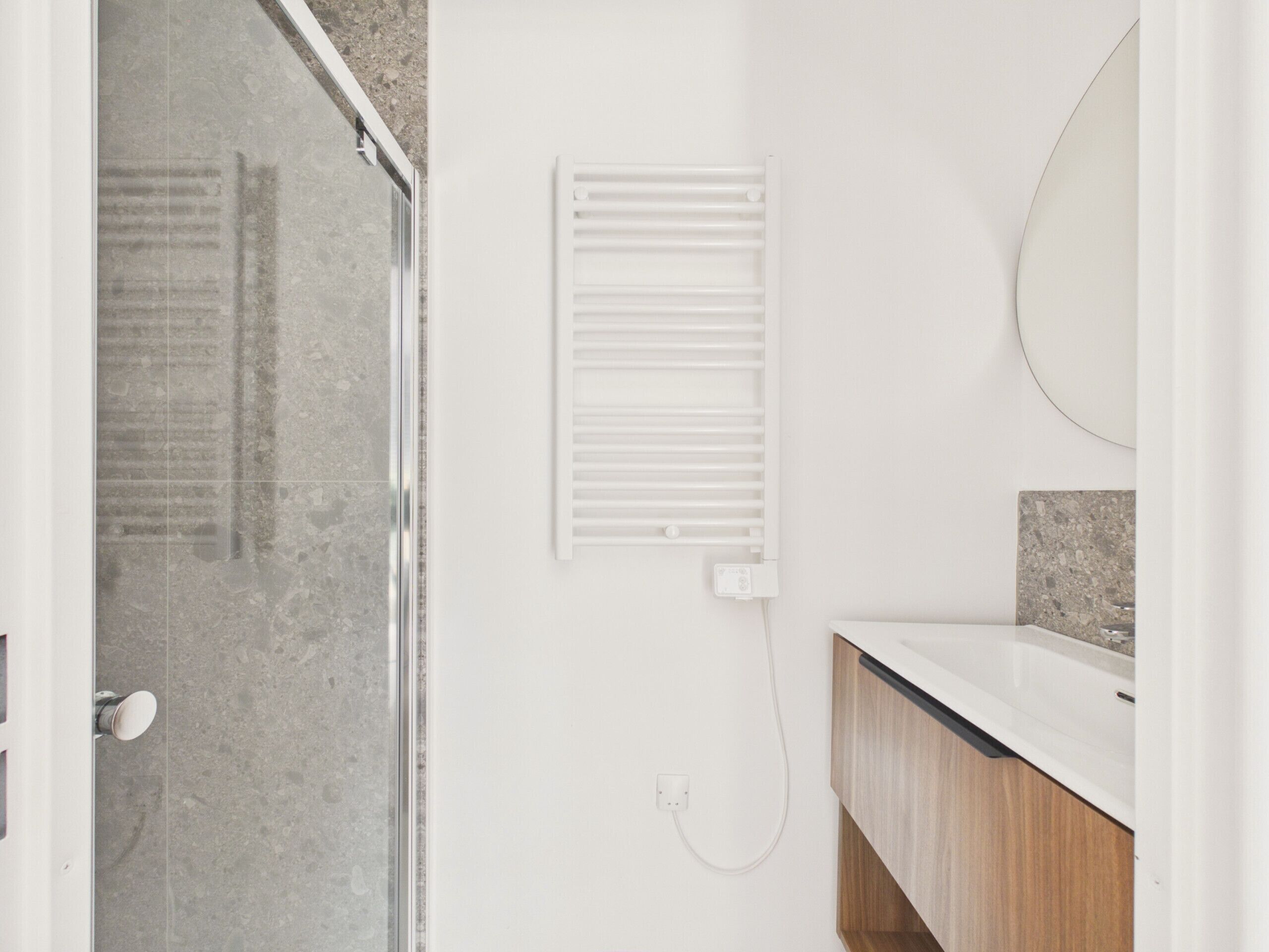 Une salle de bain avec une douche, un radiateur blanc, un miroir et un meuble en bois.