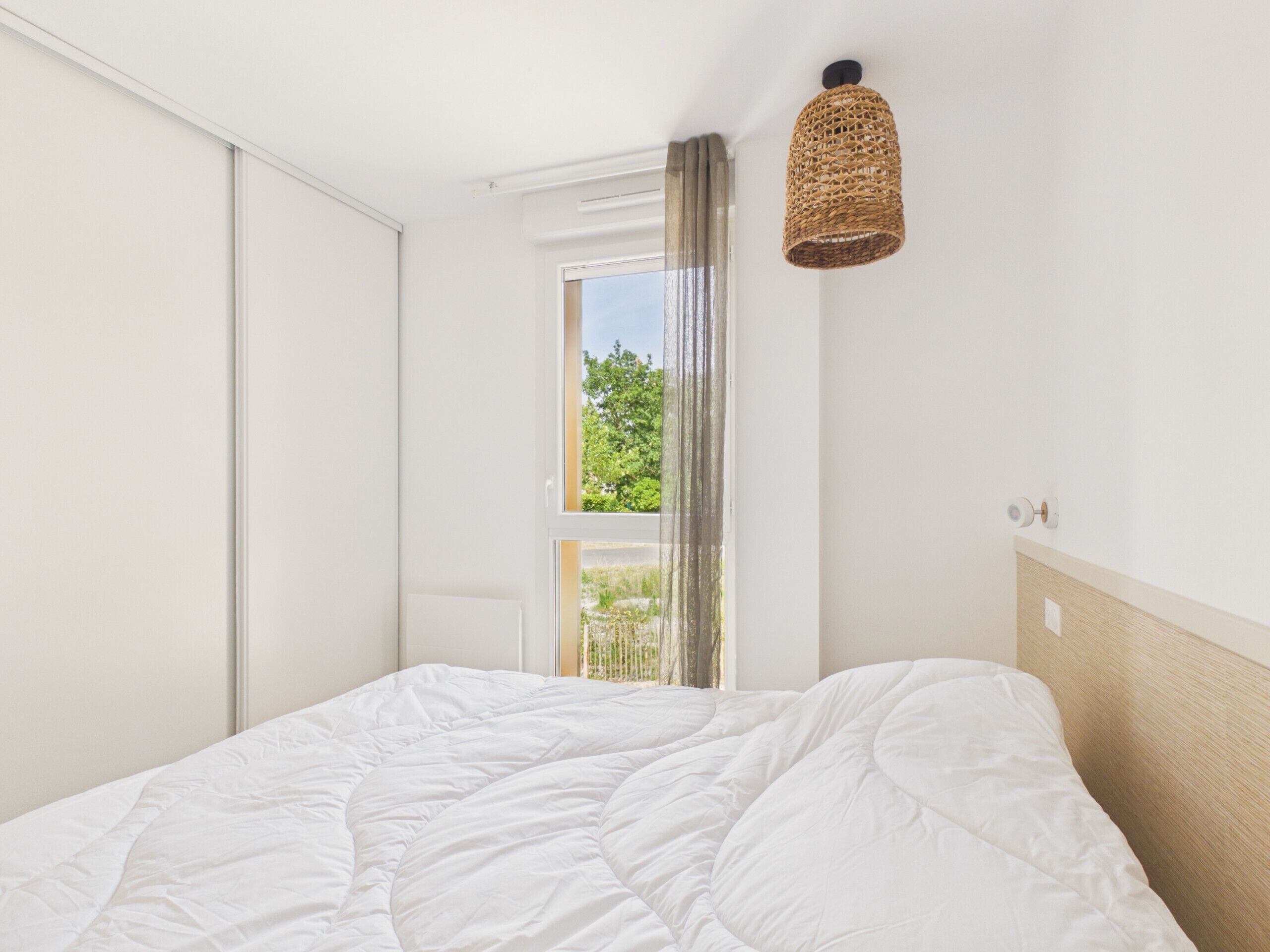 Een slaapkamer met een bed, een raam met gordijnen, een plafondlamp en een deur.