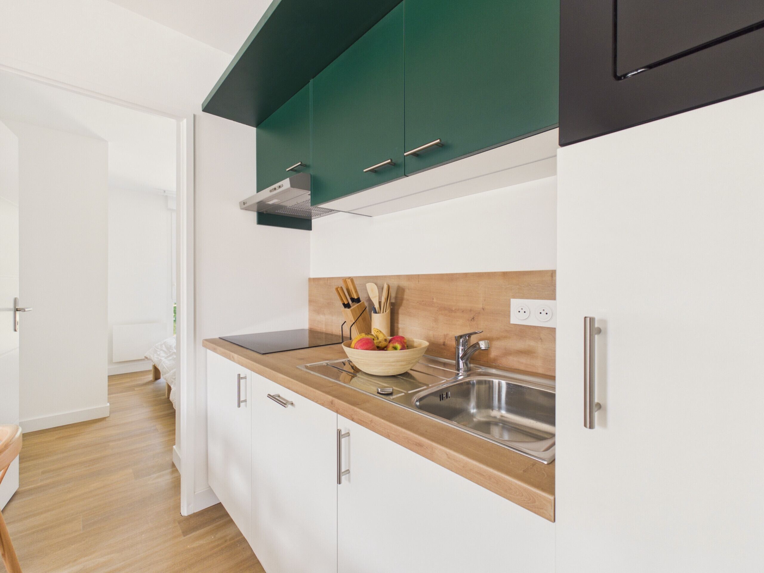 Una cocina moderna con armarios blancos, encimera de madera, pileta de acero inoxidable y salpicadero verde.