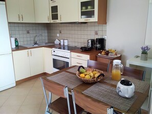 A kitchen with a stove, sink, cabinets, and a dining table with a fruit basket and a pitcher. - Casa memories (Kalligoni)