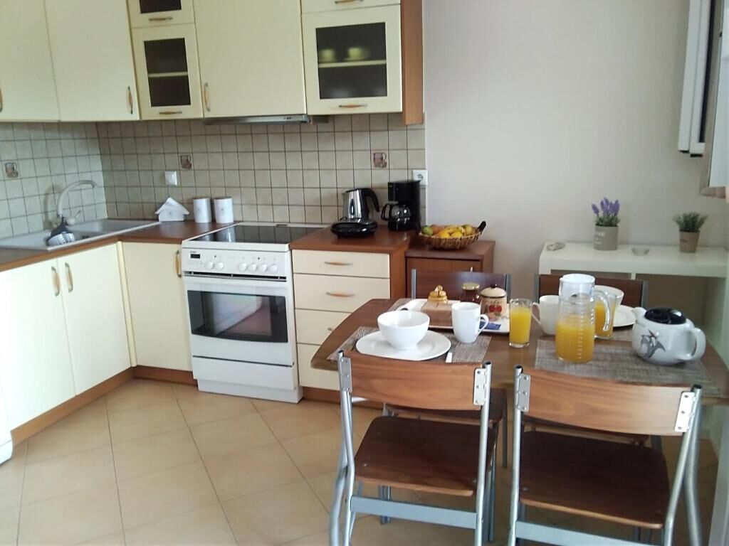 A kitchen with a stove, oven, and dining table with chairs. There is a coffee maker, a kettle, and a fruit basket on the counter.