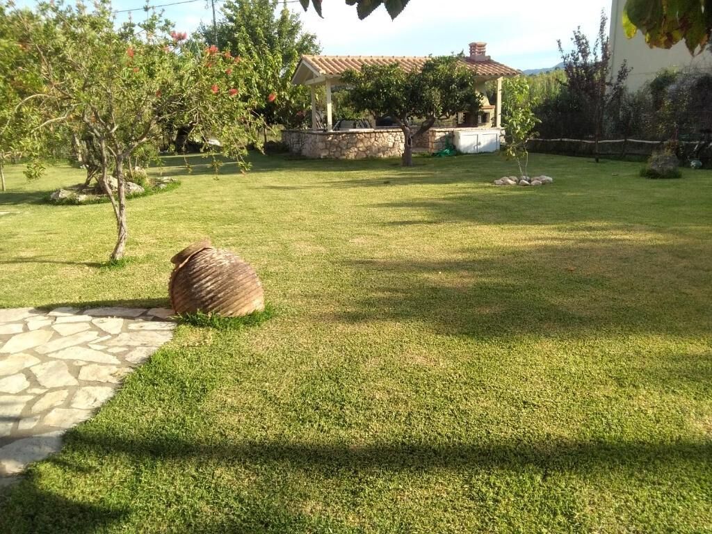 A well-maintained lawn with a stone pathway, a pergola, and a stone wall in a garden setting.