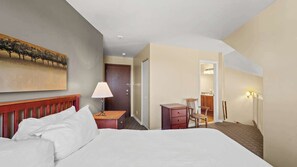 Ein Hotelzimmer mit Bett, Schreibtisch, Stuhl, Lampe, Kleiderschrank und einem Gemälde an der Wand.