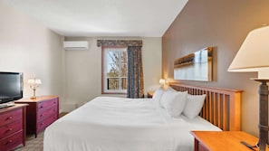 Ein Hotelzimmer mit Bett, Fernseher, Schminktisch, Fenster mit Vorhängen und einem Bild an der Wand.