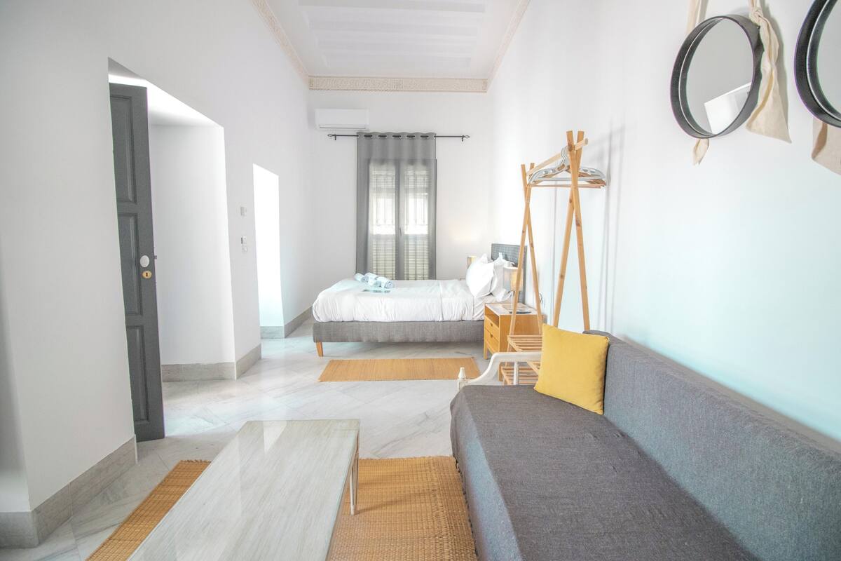 A bedroom with a bed, a sofa, a mirror, and a wardrobe.