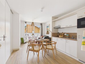 Una cucina moderna con mobili bianchi, un'area pranzo con sedie in legno e vista su un patio in legno.