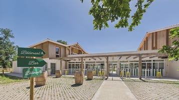 Un bâtiment doté d’une entrée couverte, de barils en bois et de panneaux indicateurs signalant « Bâtiment A » et « Bar ».