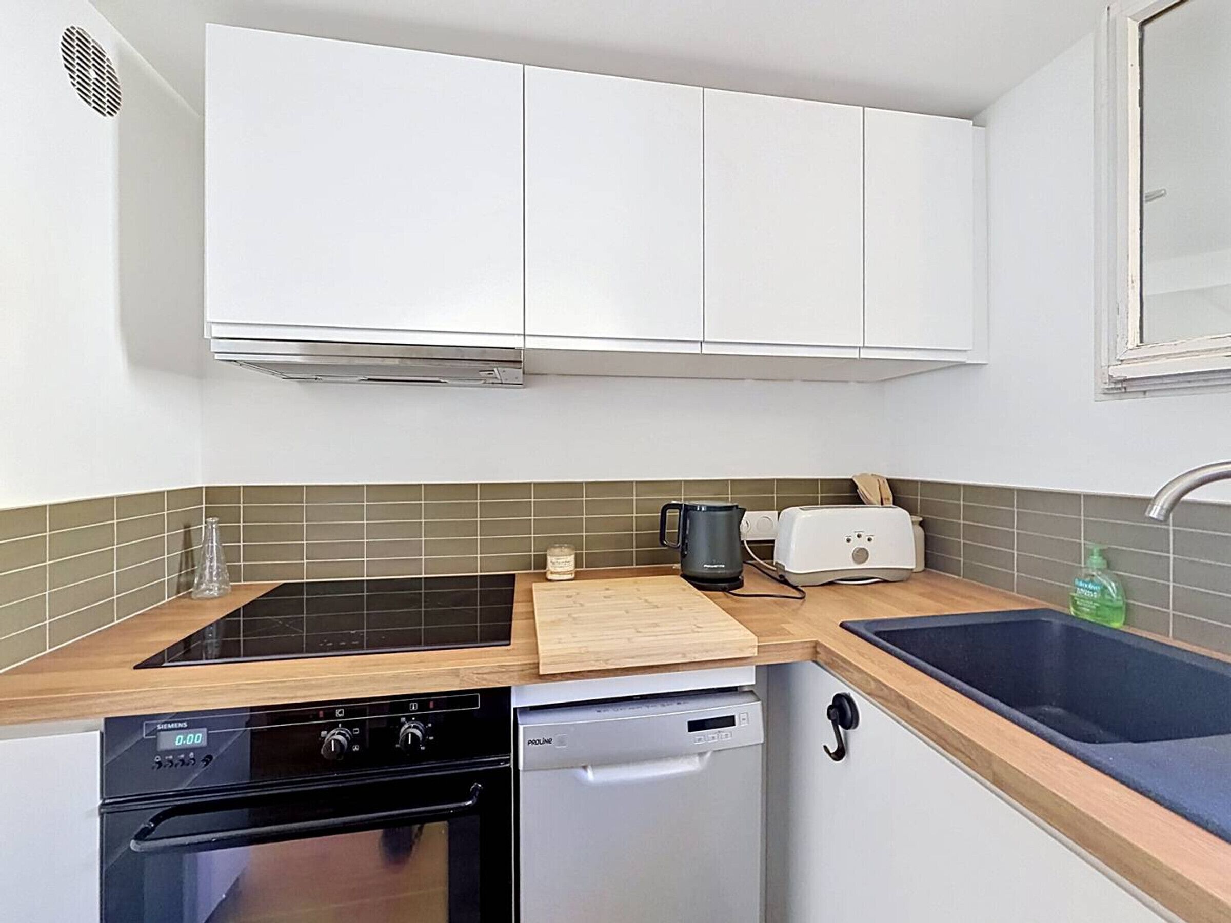 A compact kitchen with white cabinets, a black stove, a dishwasher, a wooden countertop, a toaster, and a sink.