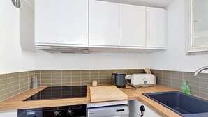 A compact kitchen with white cabinets, a black stove, a dishwasher, a wooden countertop, a toaster, and a sink. - Apartment near beach with parking - 4 guests (Saint-Cyr-sur-Mer)