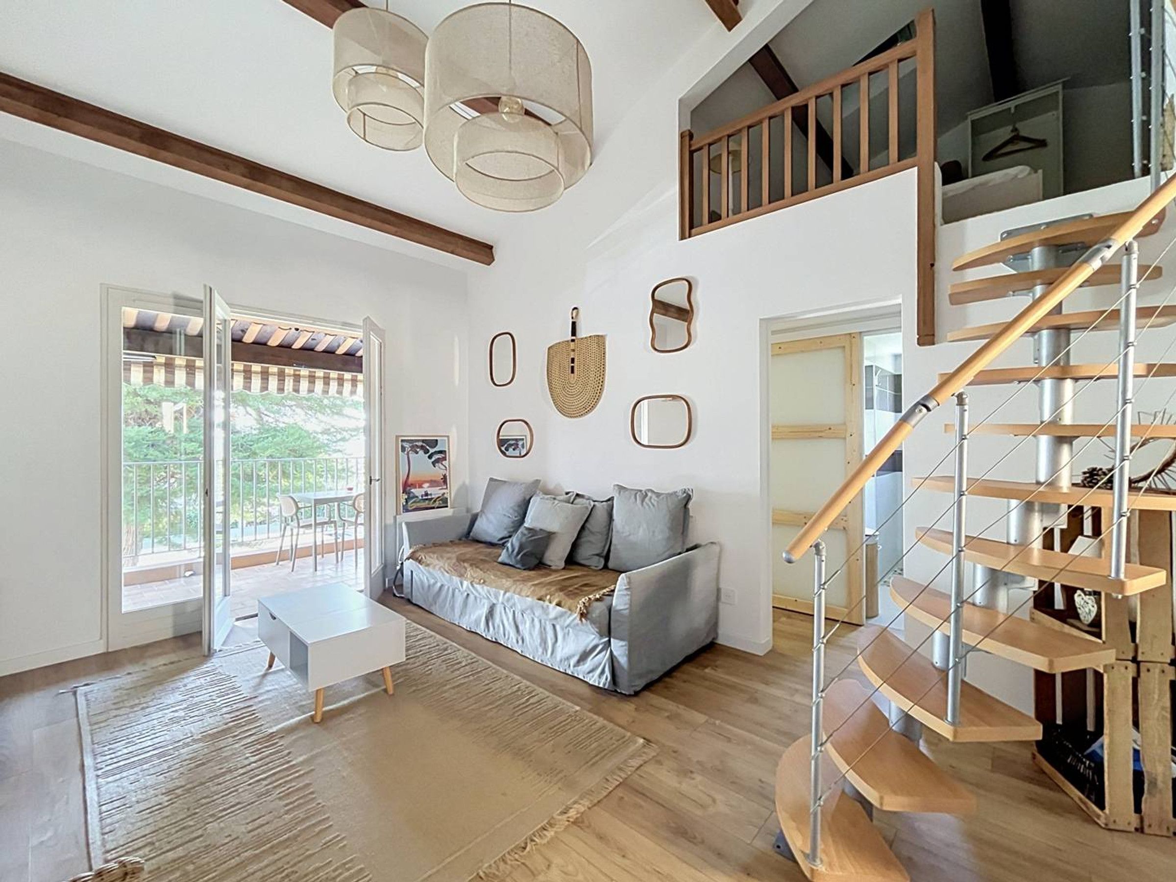 Un vaste espace de vie agrémenté d’un escalier en bois, d’un canapé, d’une table basse et offrant une vue à travers une porte vitrée.