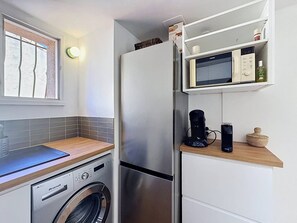 Una cocina compacta con lavadora, refrigerador, microondas y cafetera.