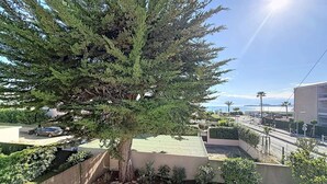 A residential area with a large tree, a paved patio, and a view of the sea. - Apartment near beach with parking - 4 guests (Saint-Cyr-sur-Mer)