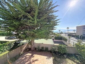 A residential area with a large tree, a paved patio, and a view of the sea. - Apartment near beach with parking - 4 guests (Saint-Cyr-sur-Mer)