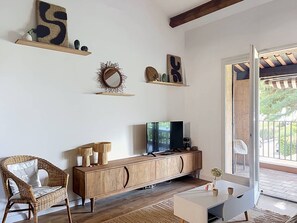Una sala de estar con un mueble de televisión de madera, una silla de mimbre y un ventanal con vistas al exterior.