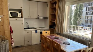 A compact kitchen with a microwave, sink, and stove, wooden dining table with chairs, and a window with a view of buildings. - Spacious apartment with balcony - 4 guests (Valloire)