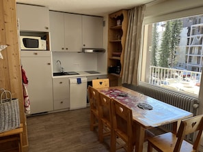 A compact kitchen with a microwave, sink, and stove, wooden dining table with chairs, and a window with a view of buildings. - Spacious apartment with balcony - 4 guests (Valloire)