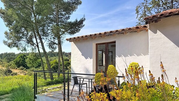Un piccolo edificio con facciata bianca e tetto in tegole, un balcone con ringhiera metallica e una porta.