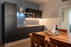 A modern kitchen with dark cabinetry, a built-in oven, and a wooden dining table with a wine bottle and glasses.