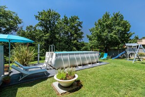 A backyard with a swimming pool, lounge chairs, a small garden, and a slide.