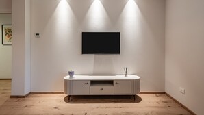 Ein modernes Wohnzimmer mit Flachbildfernseher an einer weißen Wand, einem weißen Lowboard mit Schubladen und eingelassener Beleuchtung.