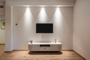 A modern living room with a flat-screen TV mounted on a white wall, a white console table with drawers, and recessed lighting.