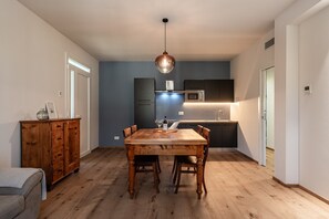 A dining area with a wooden table and chairs, a pendant light, a cabinet, and a kitchen in the background.