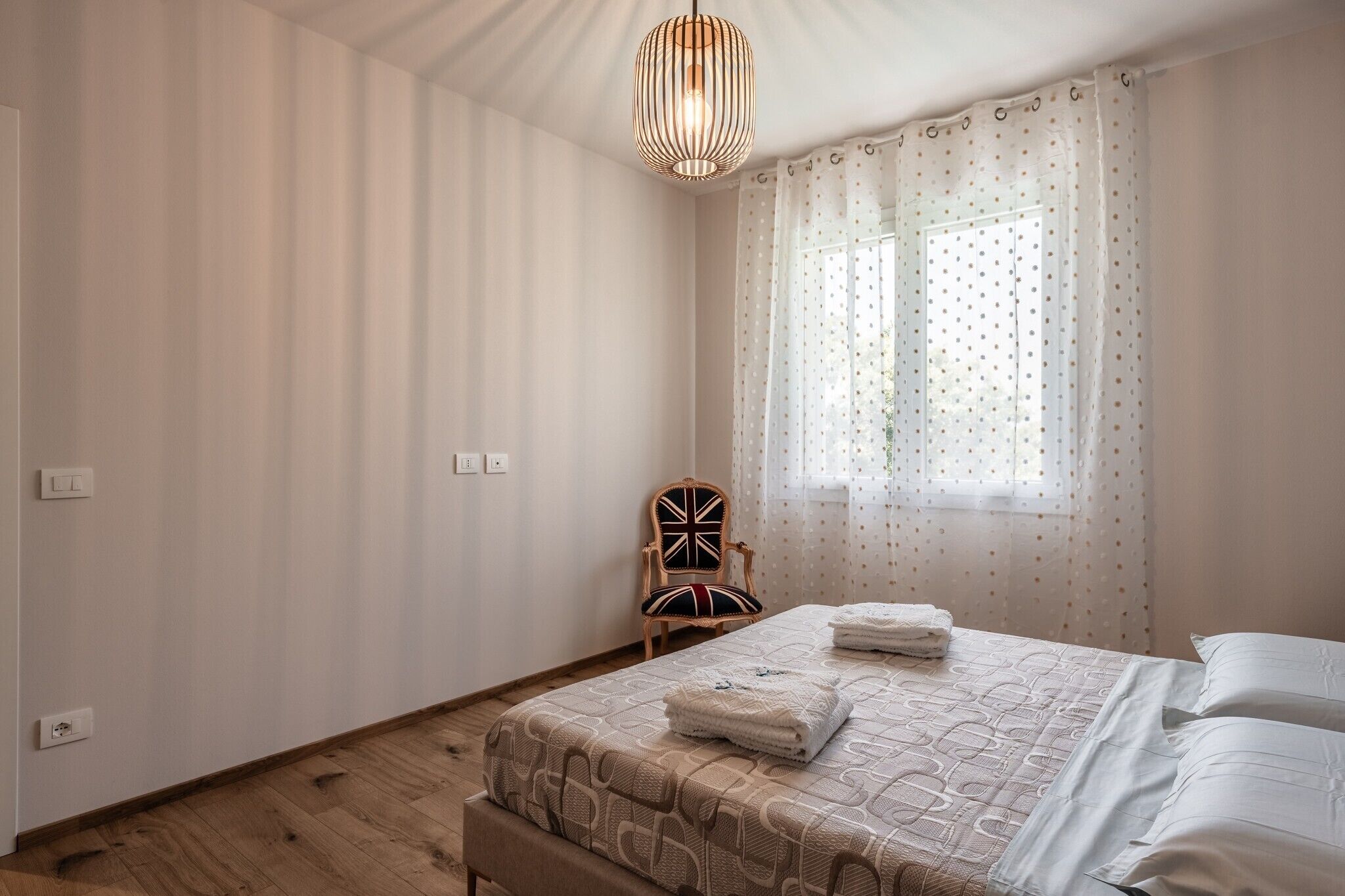 Ein Schlafzimmer mit einem Bett, einem Sessel, einem Fenster mit Vorhängen und einer Pendelleuchte.