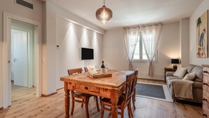 Ein Essbereich mit Holztisch, Stühlen, einer Hängelampe, einem Fernseher und einer Couch mit Decke.