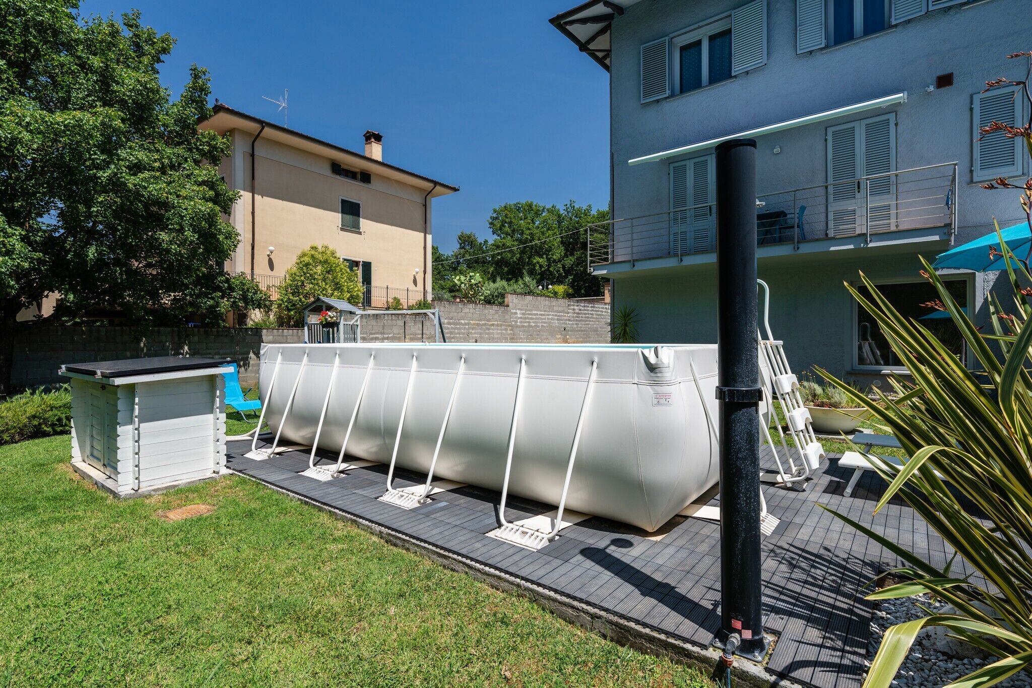 Une piscine avec un escalier, un petit abri de jardin et une zone herbeuse.